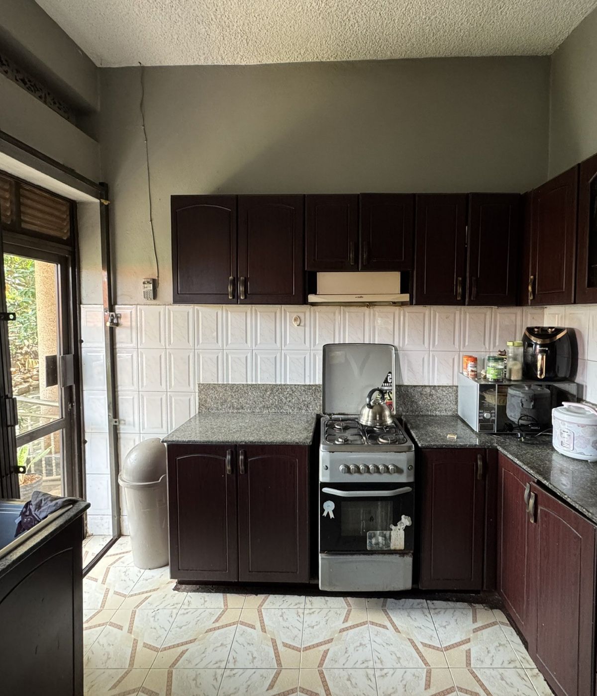 The Kanyanya kitchen before the extension: a small kitchen with dark wood cabinets, a freestanding gas cooker and patterned floor tiles.